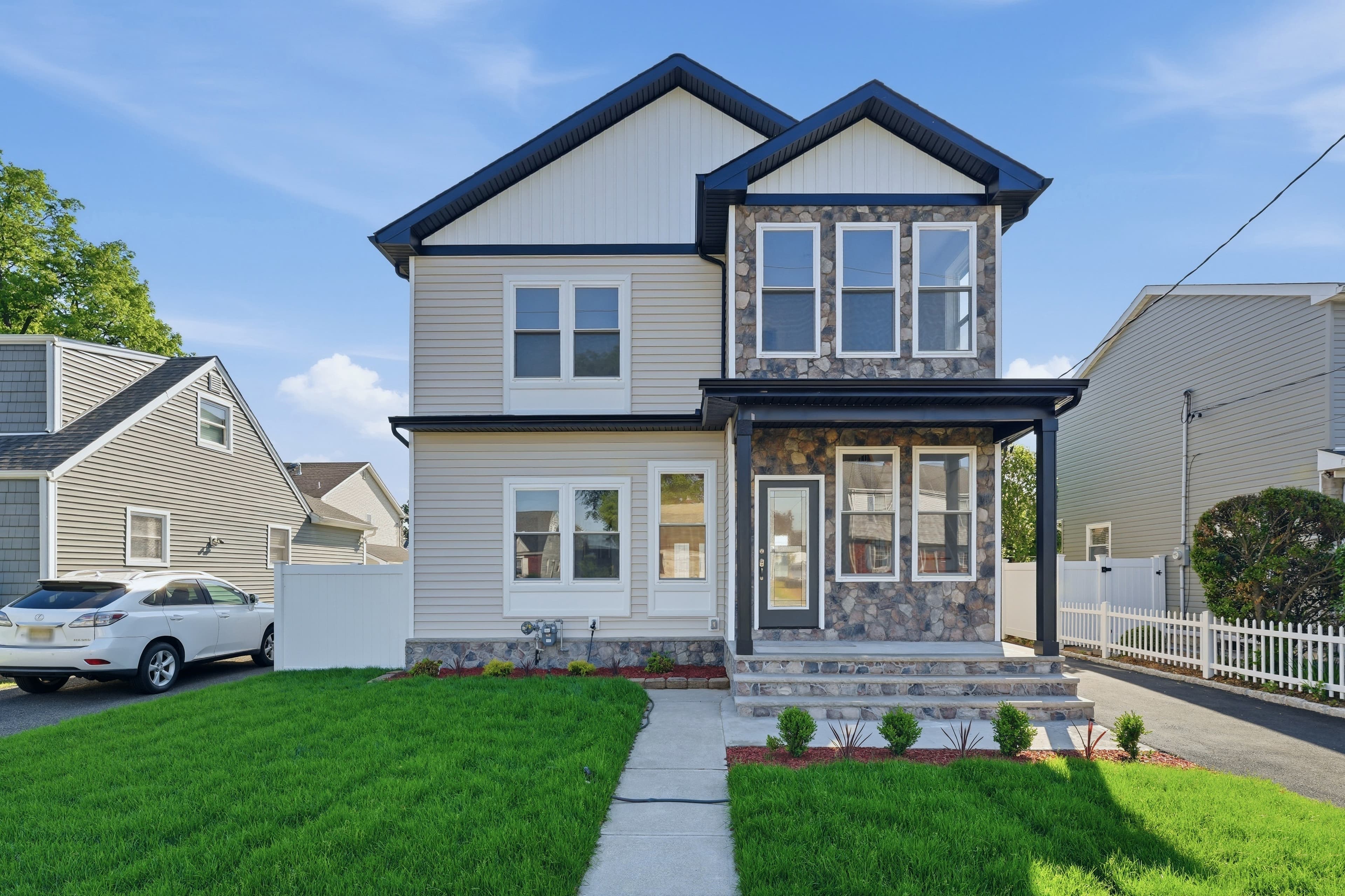 Modern two-story house with gray siding, stone accents, and green lawn under blue sky.