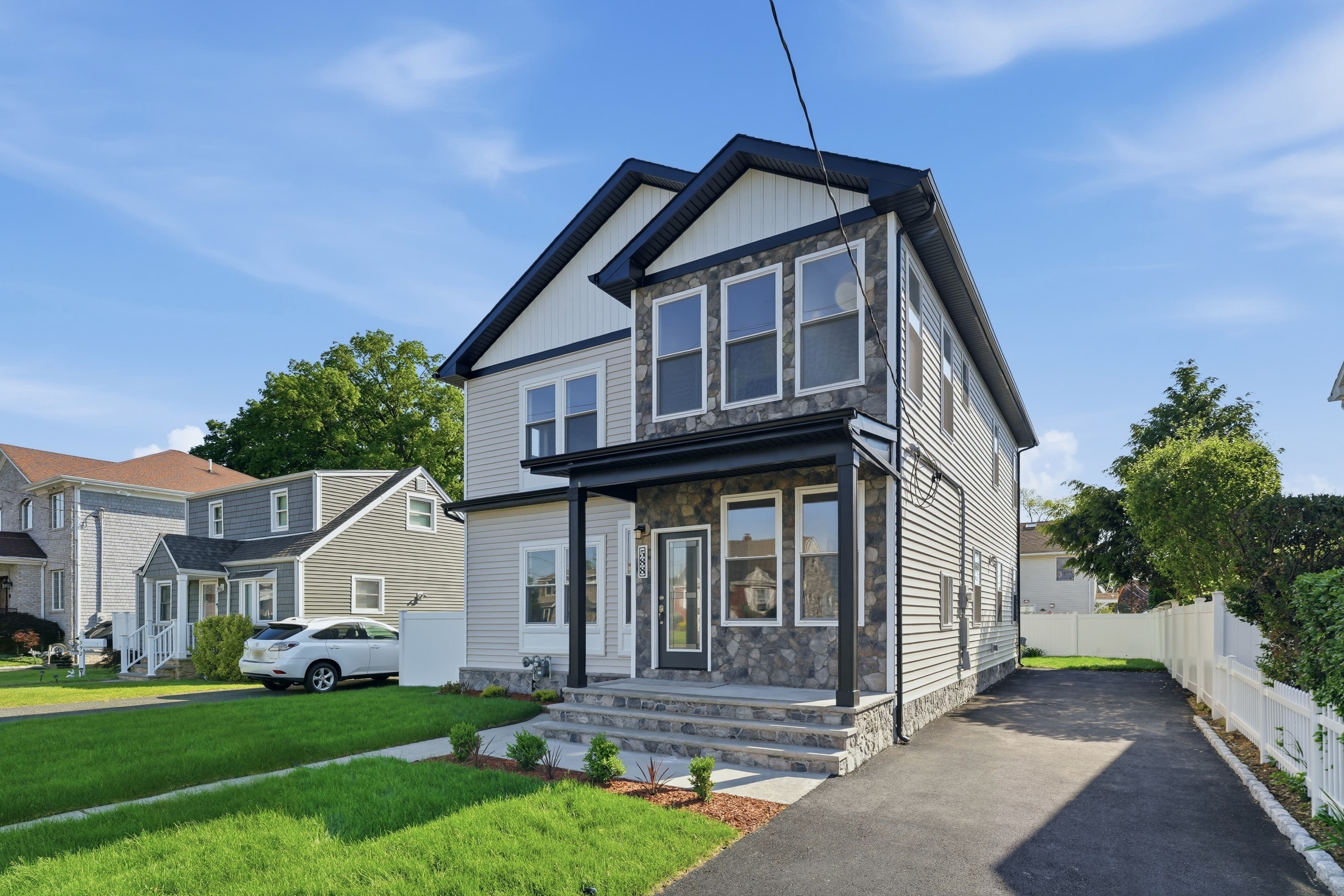 Modern two-story house with gray siding, stone accents, black trim, and a paved driveway.