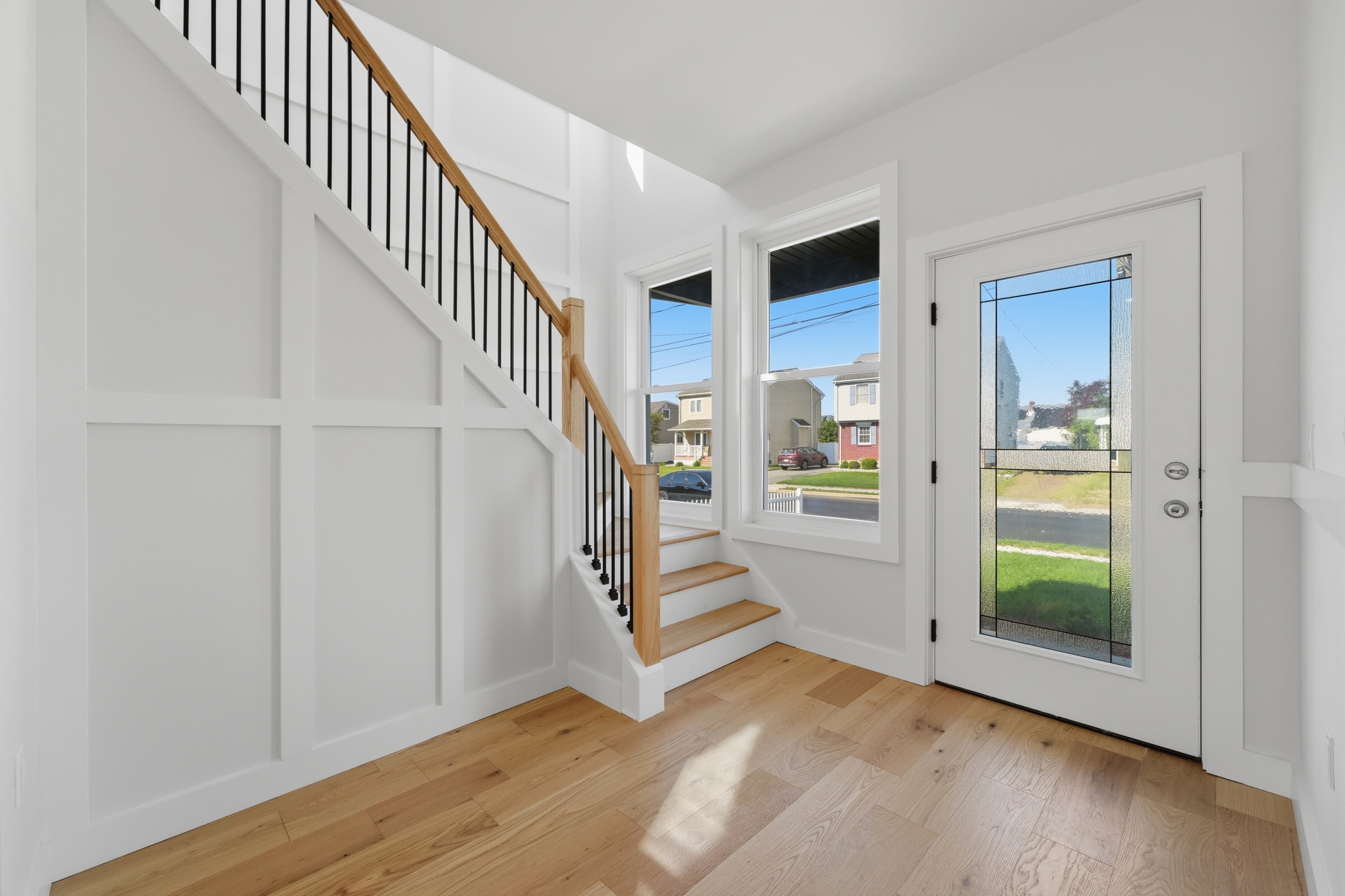 Bright entryway with white paneled walls, light wood floors, and a staircase with black spindles.