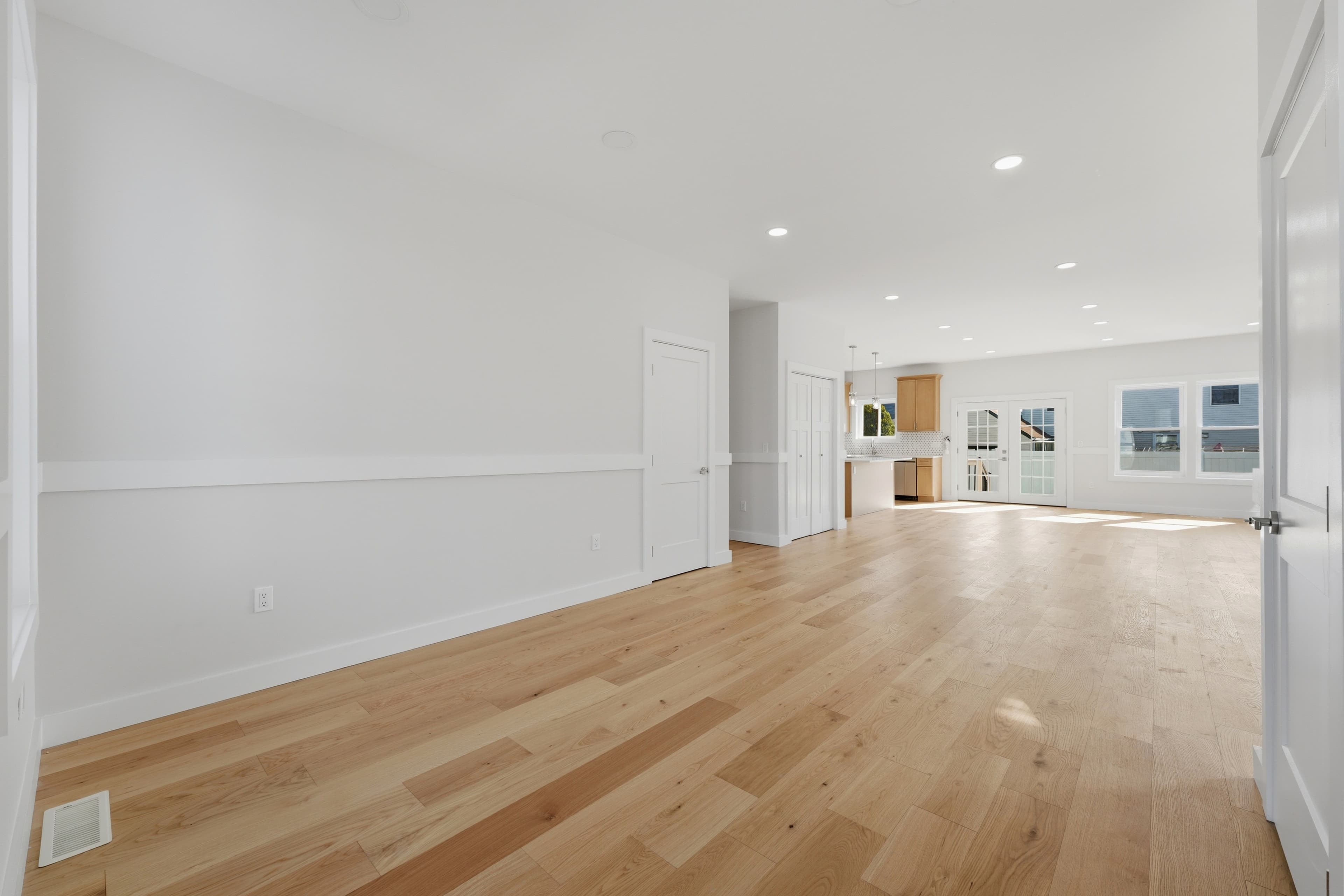 Spacious empty interior with light hardwood floors, white walls, and a modern open kitchen.