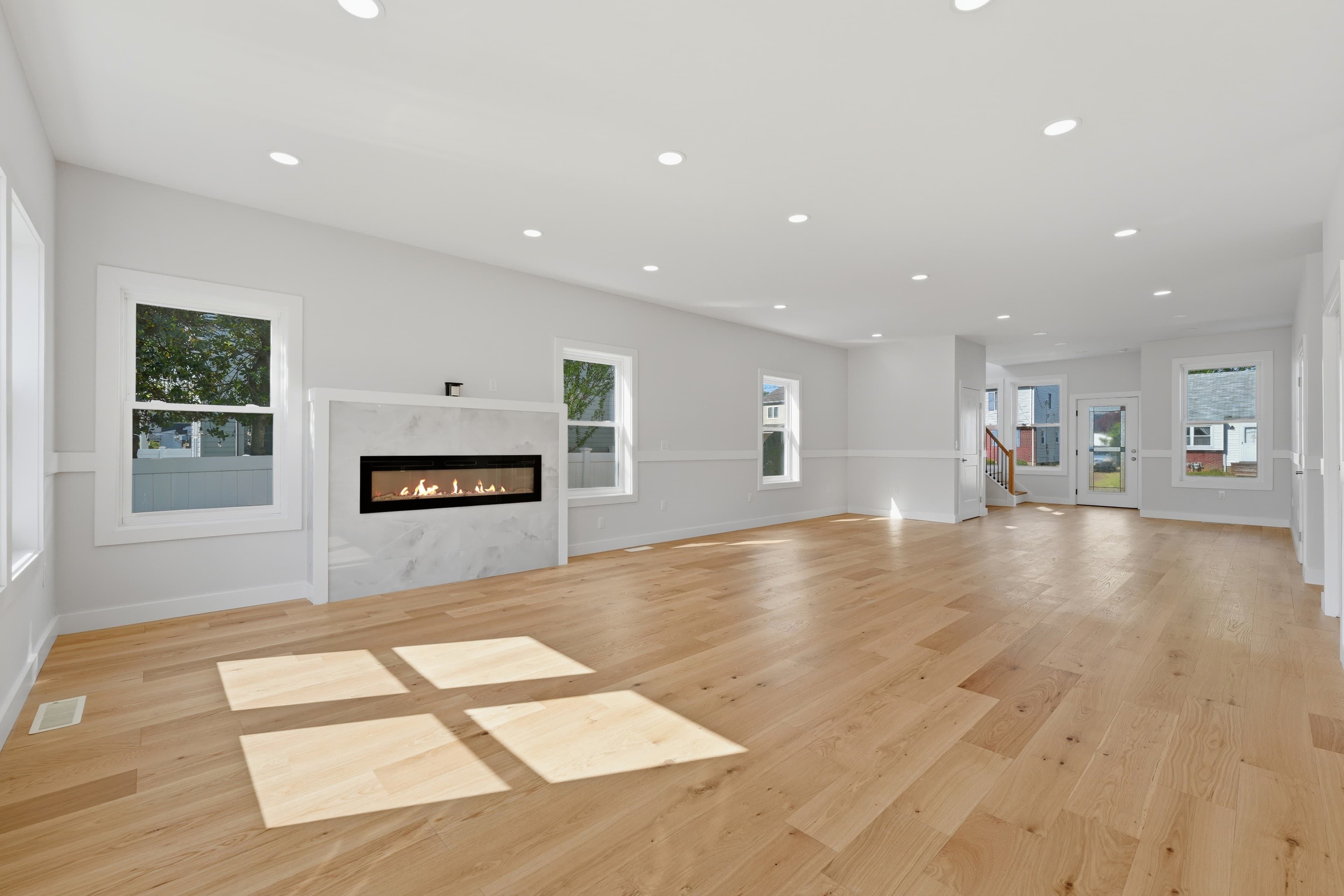 Sunlit open-concept room with light wood flooring, white walls, and a modern gas fireplace.