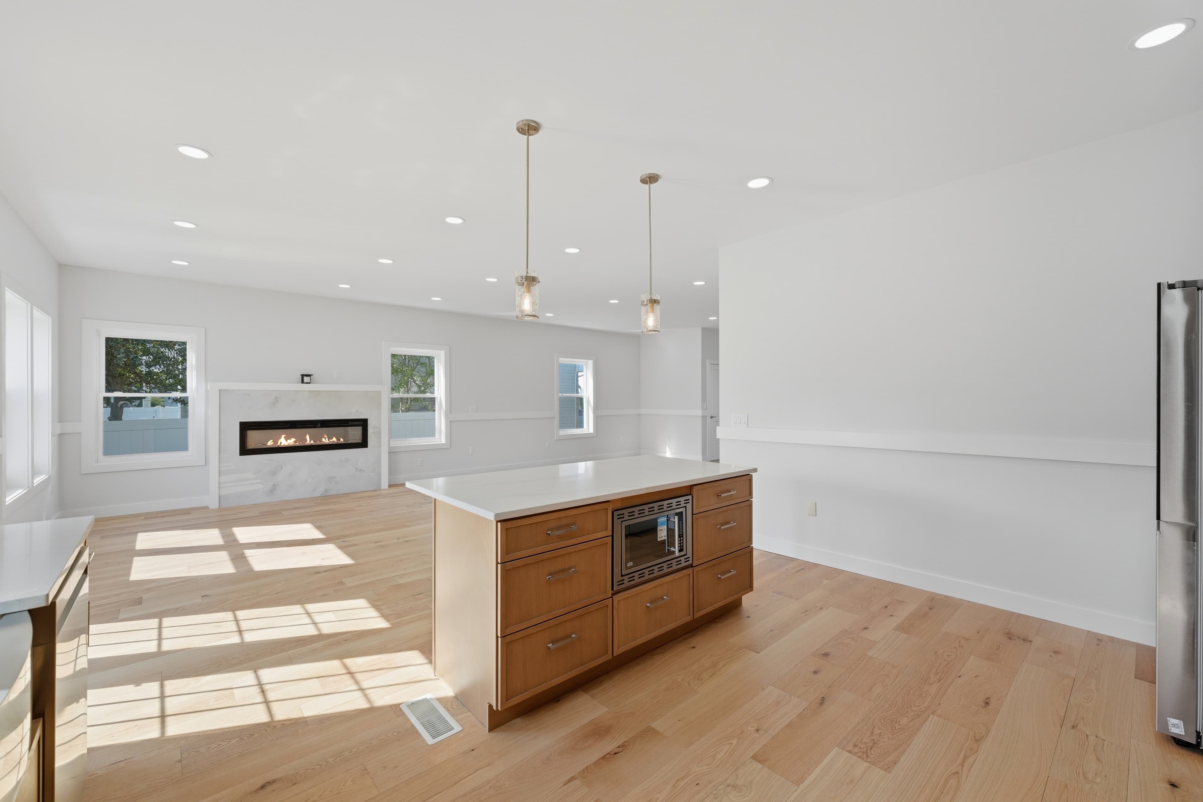 Bright open-plan living area with light wood floors, a kitchen island, and modern fireplace.