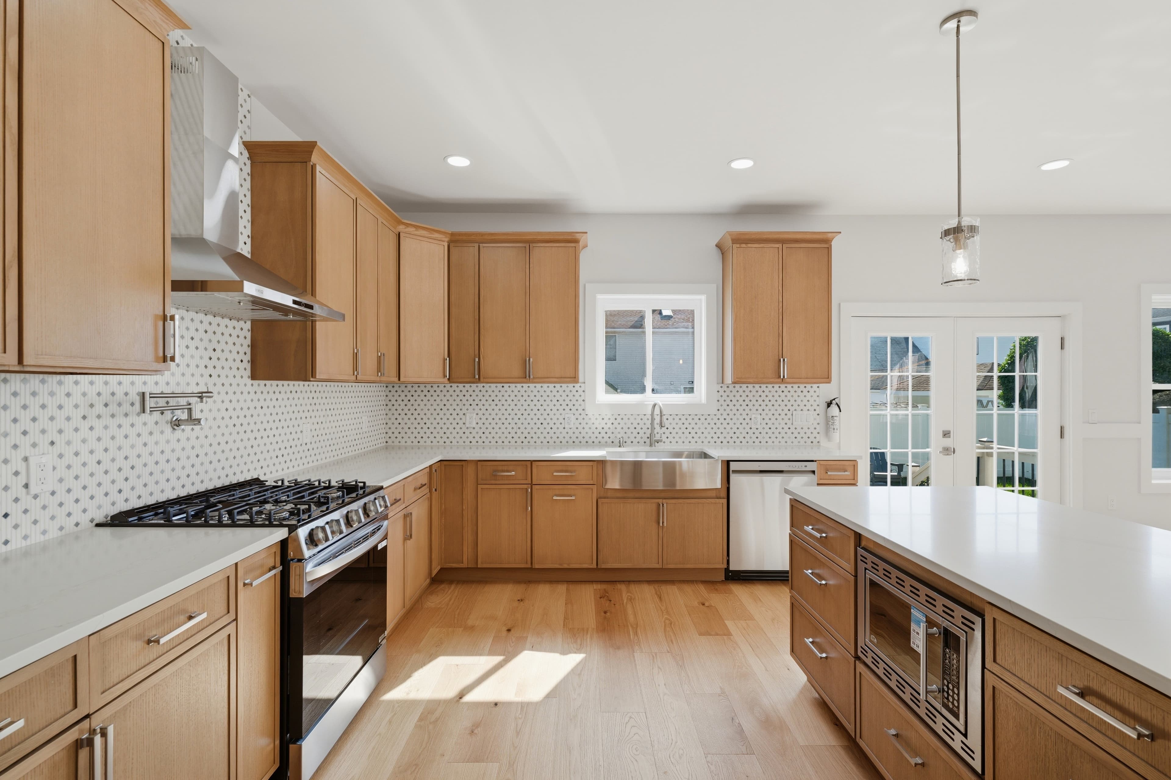 Modern kitchen with light wood cabinets, white countertops, stainless steel appliances, and a large island.