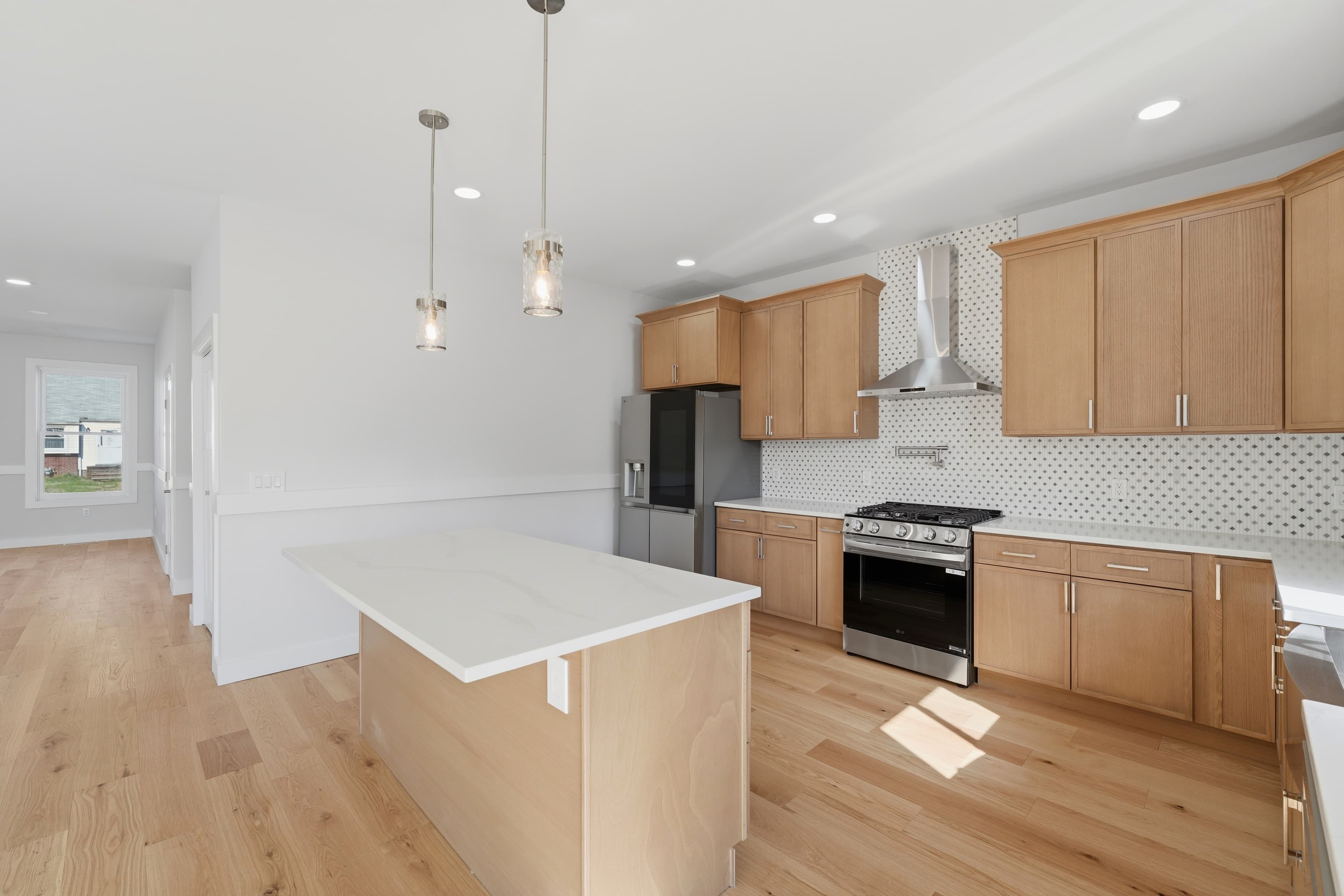 Modern kitchen with light wood cabinets, white countertops, stainless steel appliances, and a central island.