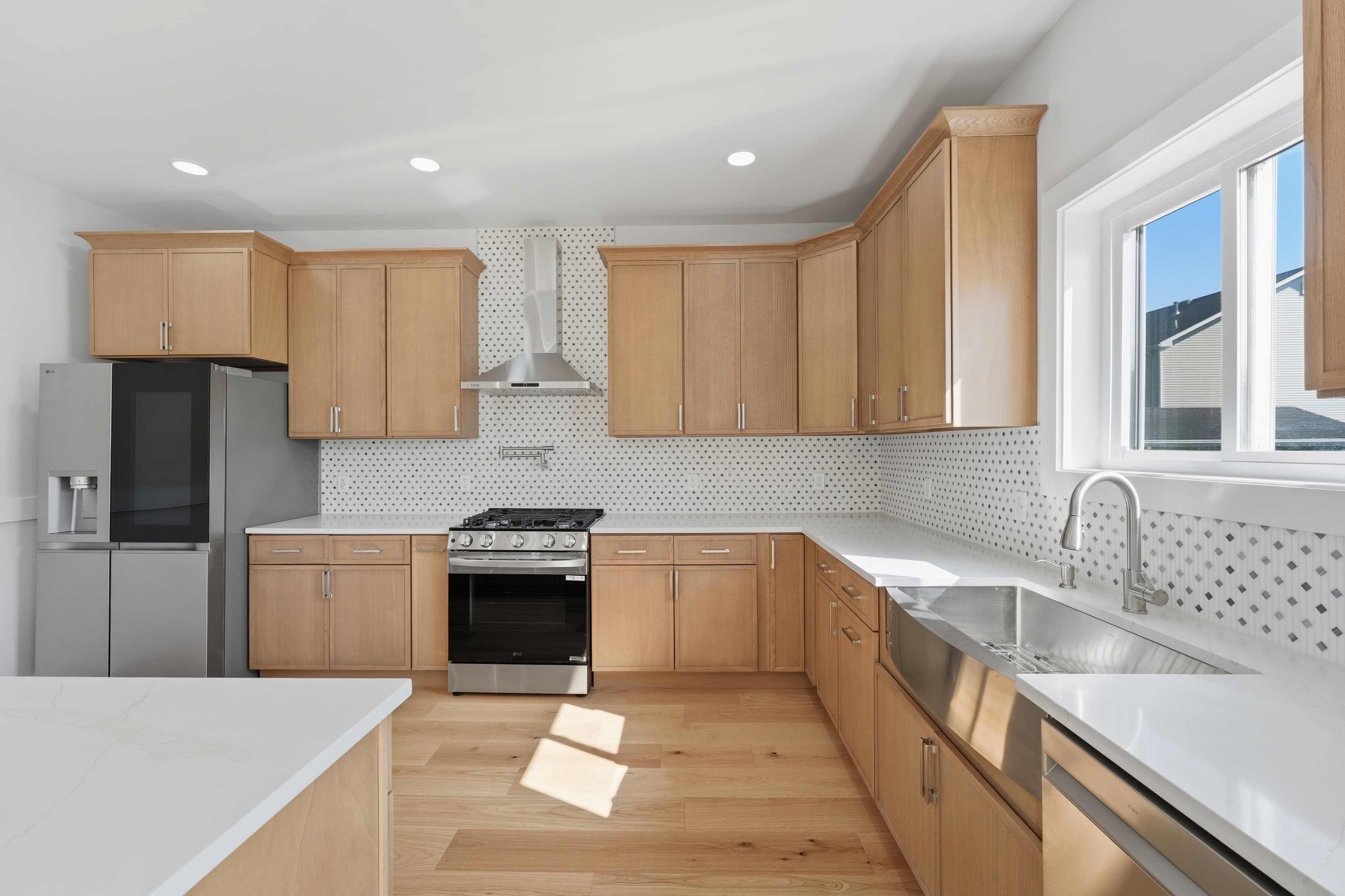 Modern kitchen featuring light wood cabinets, stainless steel appliances, white countertops, and patterned backsplash.