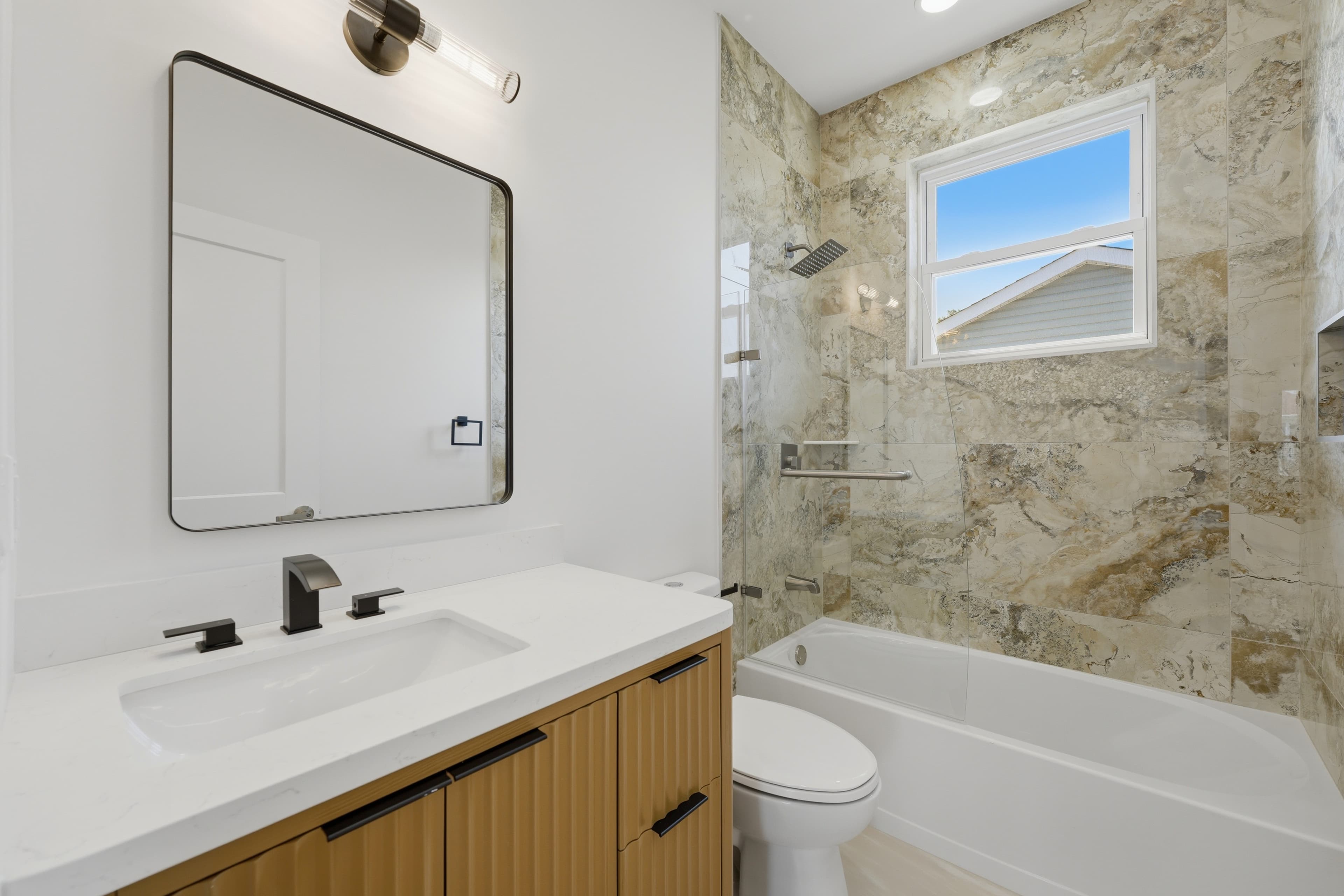 Modern bathroom featuring a wood vanity, white countertop, black fixtures, and a marble-tiled shower.